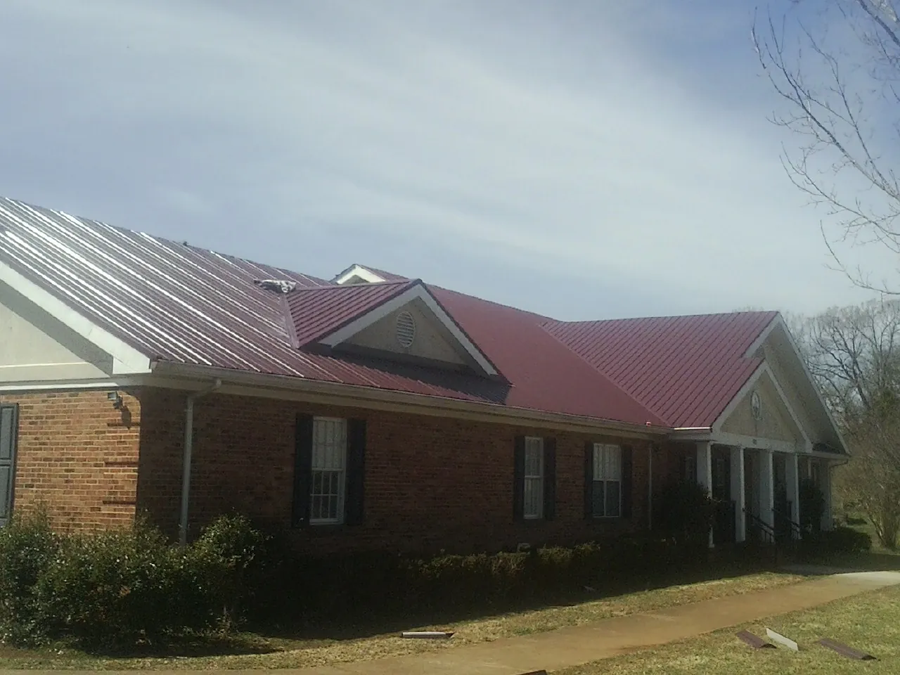 Red metal roof with gabled entries on a long brick building, from a Hail Damage Roof Repair job in Hampton